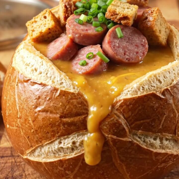 A close-up of a ladle lifting thick, molten beer cheese soup with bratwurst coins and melted cheese.