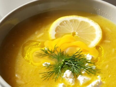 A steaming bowl of creamy Greek lemon chicken orzo soup garnished with fresh dill, feta, and a lemon slice.