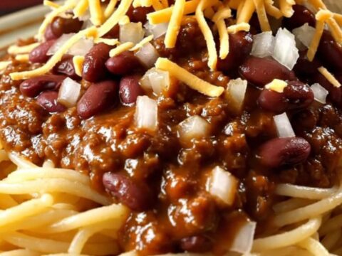 A close-up view of a ladle lifting rich, mahogany-colored Cincinnati chili from a red ceramic slow cooker.