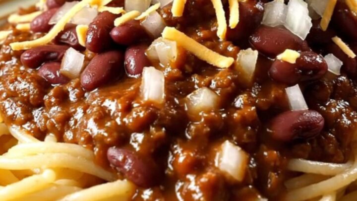 A close-up view of a ladle lifting rich, mahogany-colored Cincinnati chili from a red ceramic slow cooker.
