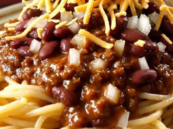 A close-up view of a ladle lifting rich, mahogany-colored Cincinnati chili from a red ceramic slow cooker.