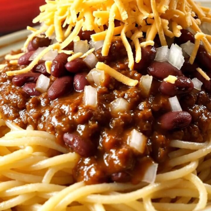 A close-up view of a ladle lifting rich, mahogany-colored Cincinnati chili from a red ceramic slow cooker.