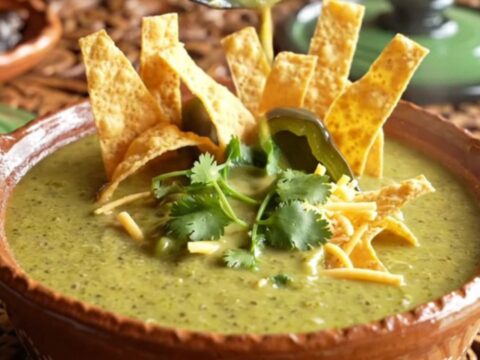 A close-up of a rustic clay bowl filled with vibrant green poblano and chicken cream soup.