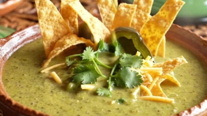 A close-up of a rustic clay bowl filled with vibrant green poblano and chicken cream soup.