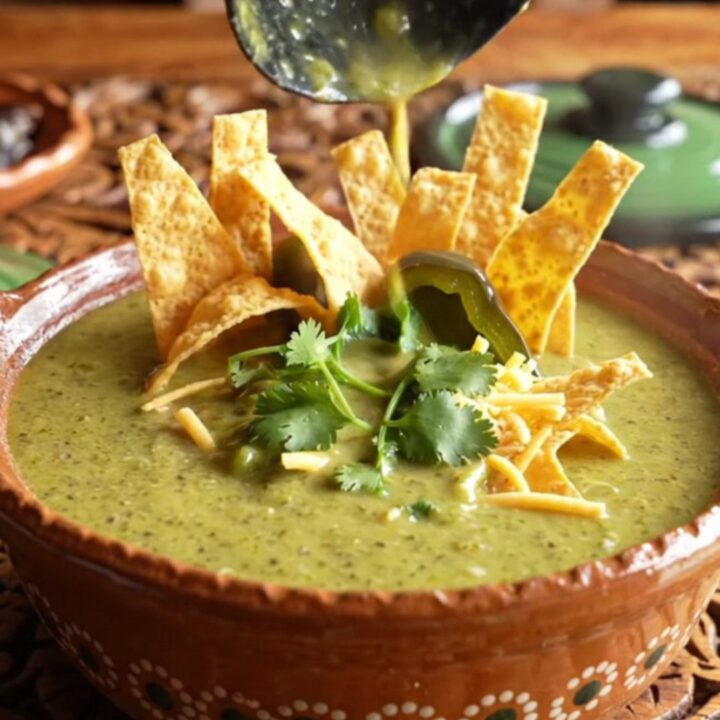 A close-up of a rustic clay bowl filled with vibrant green poblano and chicken cream soup.