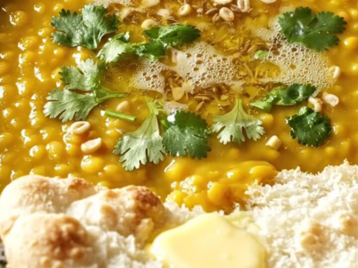A golden, velvety red lentil dal served in a ceramic bowl, topped with cilantro and cumin-infused ghee.