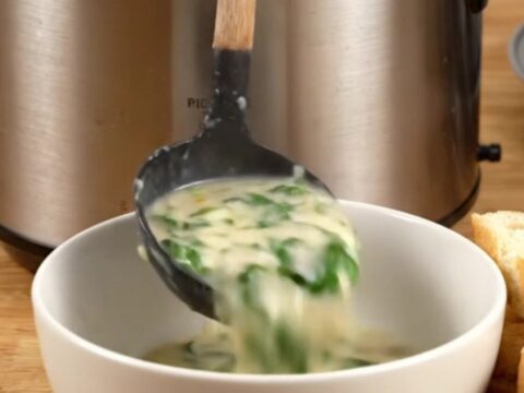 Creamy spinach artichoke chicken served in a ceramic bowl with toasted baguette slices on the side.
