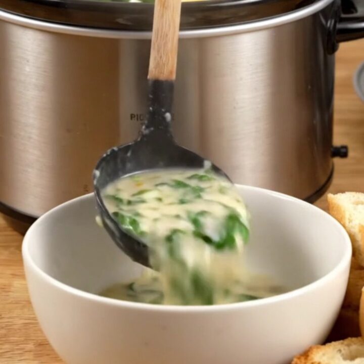 Creamy spinach artichoke chicken served in a ceramic bowl with toasted baguette slices on the side.