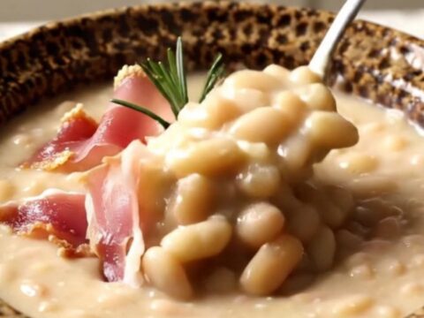 A rustic ceramic bowl filled with velvety white bean soup topped with crispy prosciutto and fresh rosemary.
