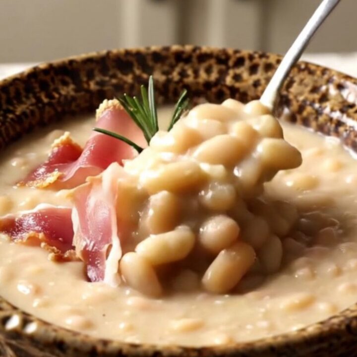 A rustic ceramic bowl filled with velvety white bean soup topped with crispy prosciutto and fresh rosemary.