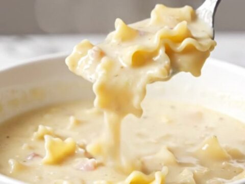 A bowl of creamy white lasagna soup with sausage, noodles, and spinach.