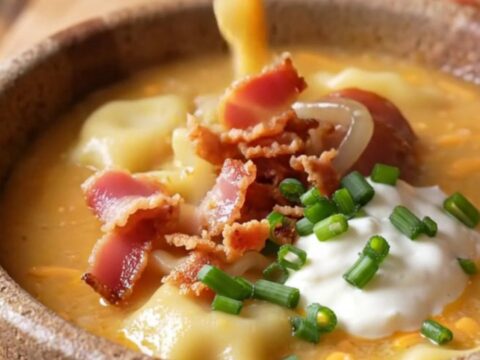 A rustic bowl of creamy pierogi soup topped with crispy bacon, caramelized onions, and fresh chives