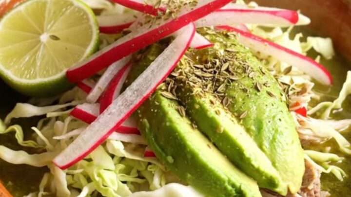 A warm clay bowl filled with vibrant green Pozole Verde, topped with fresh radish, cabbage, avocado, and lime.