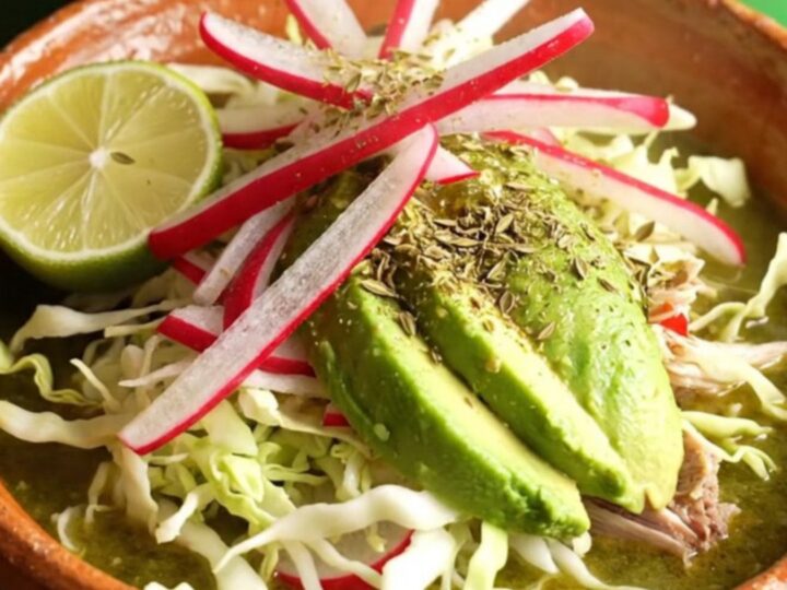 A warm clay bowl filled with vibrant green Pozole Verde, topped with fresh radish, cabbage, avocado, and lime.