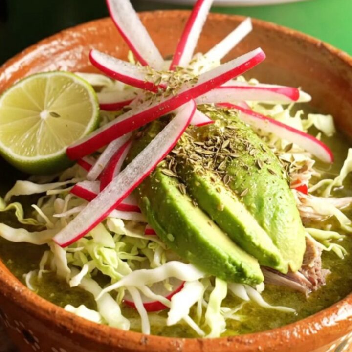 A warm clay bowl filled with vibrant green Pozole Verde, topped with fresh radish, cabbage, avocado, and lime.