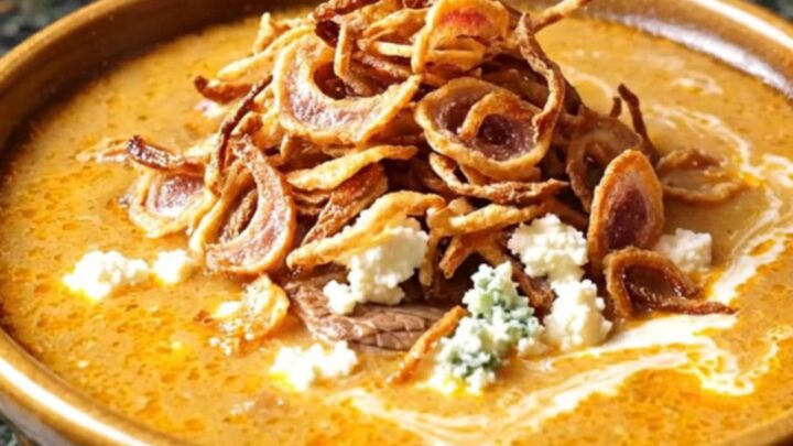 A close-up of a ladle lifting rich, creamy buffalo steak chowder from a dark stoneware Crockpot.
