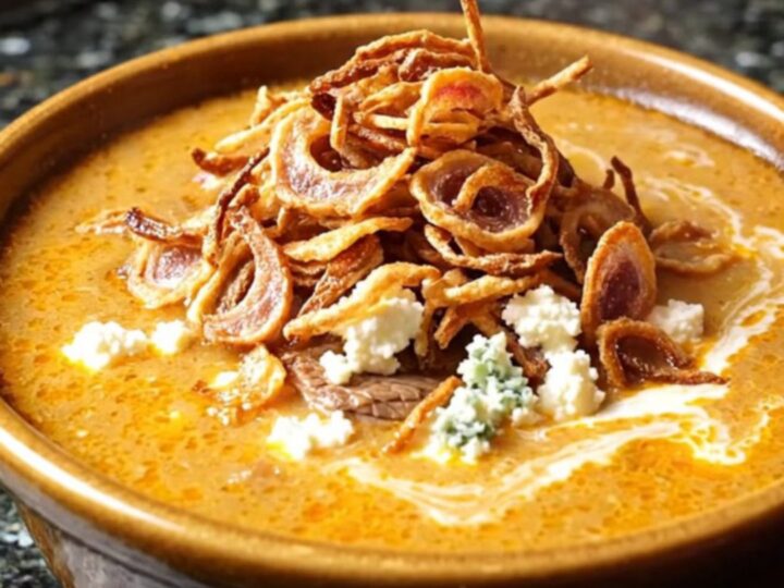 A close-up of a ladle lifting rich, creamy buffalo steak chowder from a dark stoneware Crockpot.