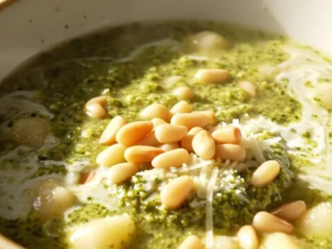 A bowl of creamy basil pesto chicken gnocchi soup topped with mozzarella pearls and pine nuts.