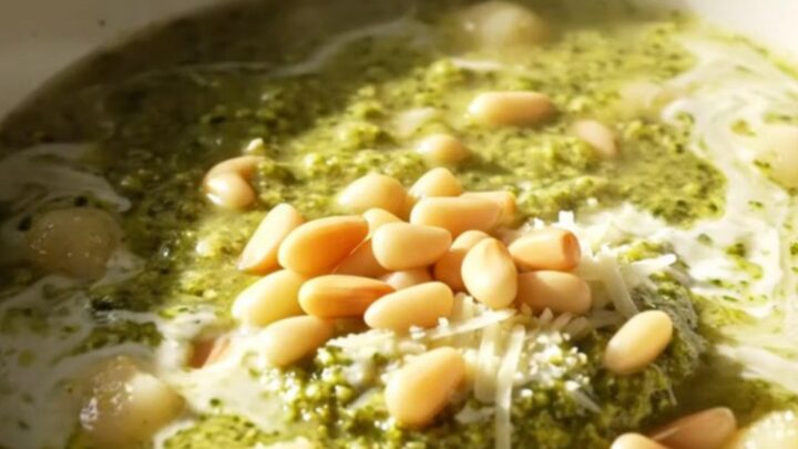 A bowl of creamy basil pesto chicken gnocchi soup topped with mozzarella pearls and pine nuts.
