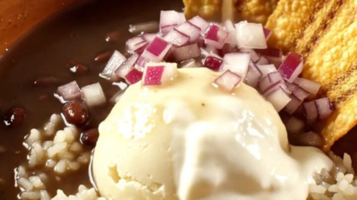 A warm ceramic bowl of glossy black bean soup with a swirl of crema and ham chunks.