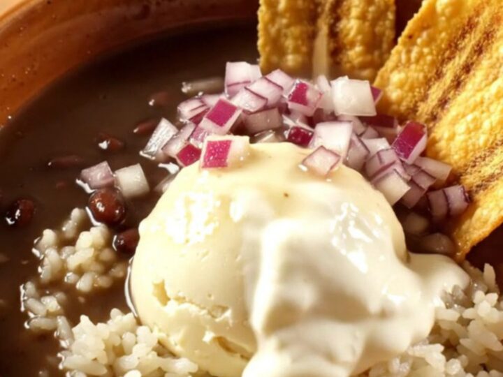 A warm ceramic bowl of glossy black bean soup with a swirl of crema and ham chunks.