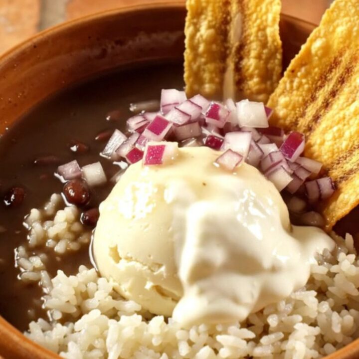 A warm ceramic bowl of glossy black bean soup with a swirl of crema and ham chunks.