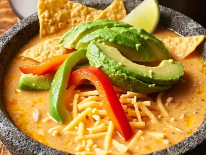 A warm stoneware bowl filled with creamy fajita chicken soup topped with avocado, lime, and tortilla strips.