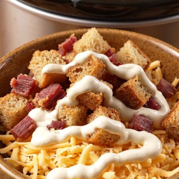 A warm ceramic bowl filled with creamy Reuben chowder, topped with rye croutons and a swirl of dressing.