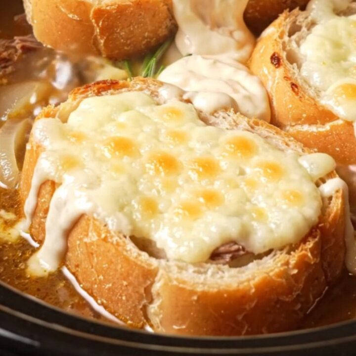 A deep stoneware crock filled with rich French dip soup topped with a golden, bubbly Gruyere cheese baguette slice.
