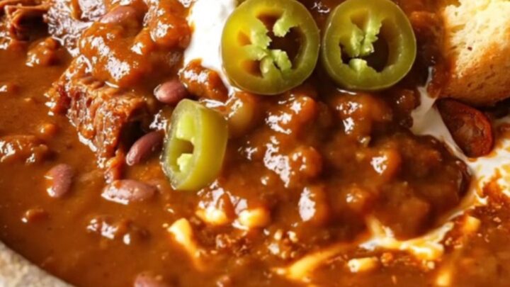 A rustic stoneware bowl filled with rich, mahogany-colored seven-bean chili topped with cilantro and sour cream.