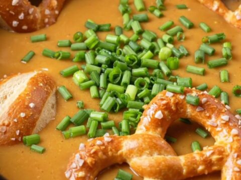 A warm, bubbling pot of creamy beer cheese dip served in a rustic crockpot with soft pretzel bites.