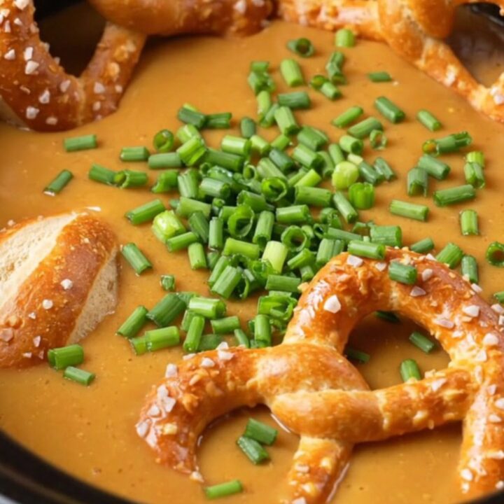 A warm, bubbling pot of creamy beer cheese dip served in a rustic crockpot with soft pretzel bites.
