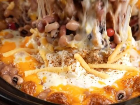 A macro shot of a tortilla chip scooping into a bubbling, cheesy, bean-filled dip inside a red slow cooker.