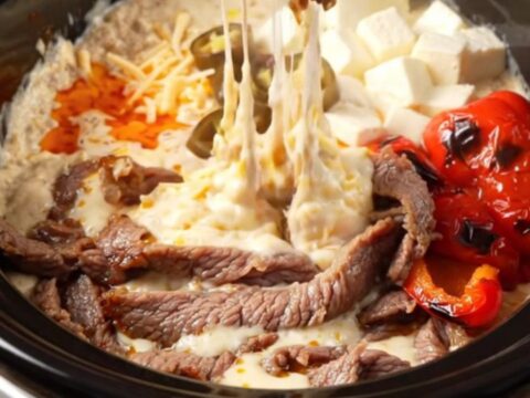 A close-up of a crispy tortilla strip being dipped into a creamy, bubbling steak fajita queso dip in a ceramic slow cooker.