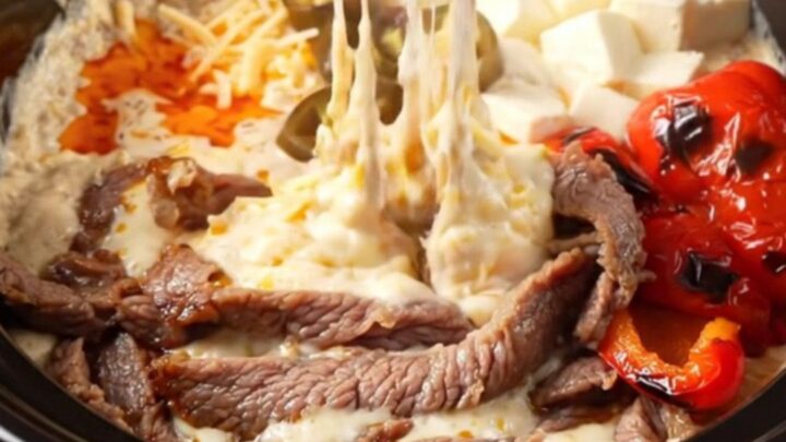 A close-up of a crispy tortilla strip being dipped into a creamy, bubbling steak fajita queso dip in a ceramic slow cooker.