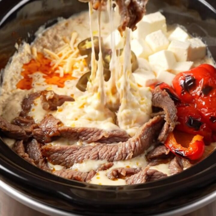 A close-up of a crispy tortilla strip being dipped into a creamy, bubbling steak fajita queso dip in a ceramic slow cooker.