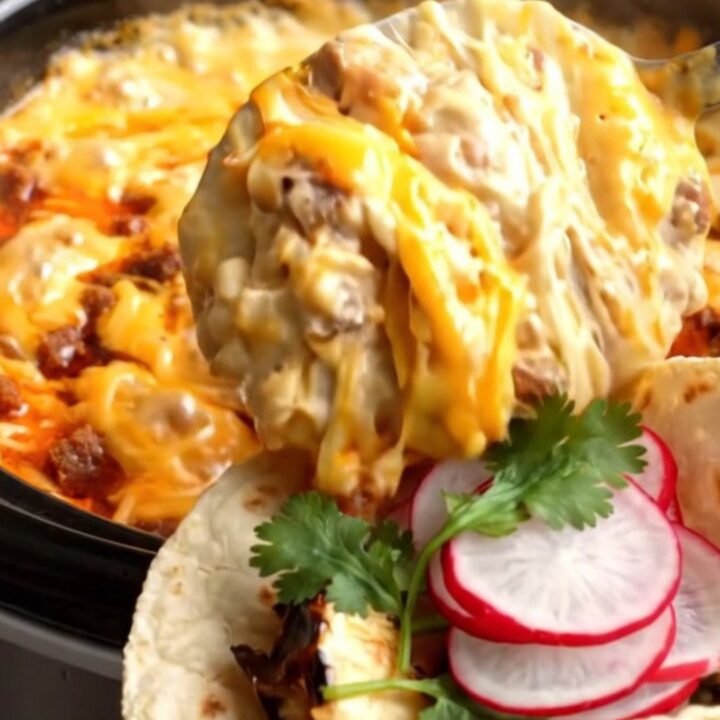 A close-up shot of a molten cheese pull from a dark ceramic Crockpot filled with chorizo and poblano fundido.