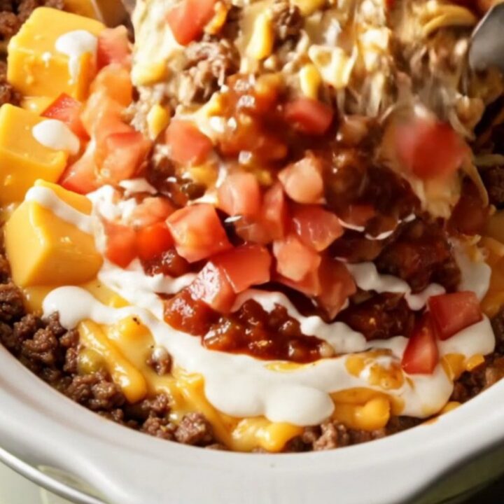 A close-up of a tortilla scoop plunging into a bubbling, creamy taco queso dip in a white Crockpot.