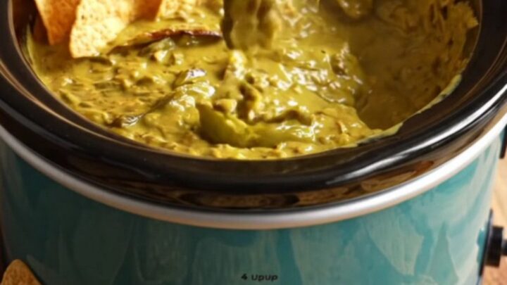 A close-up of a corn tortilla chip being dipped into a bubbling, golden-green Hatch chile and smoked cheddar queso dip.