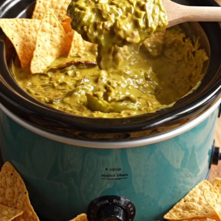 A close-up of a corn tortilla chip being dipped into a bubbling, golden-green Hatch chile and smoked cheddar queso dip.