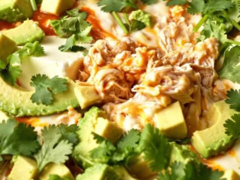 A close-up of a creamy chicken enchilada dip in a terracotta Crockpot with a dramatic cheese pull.