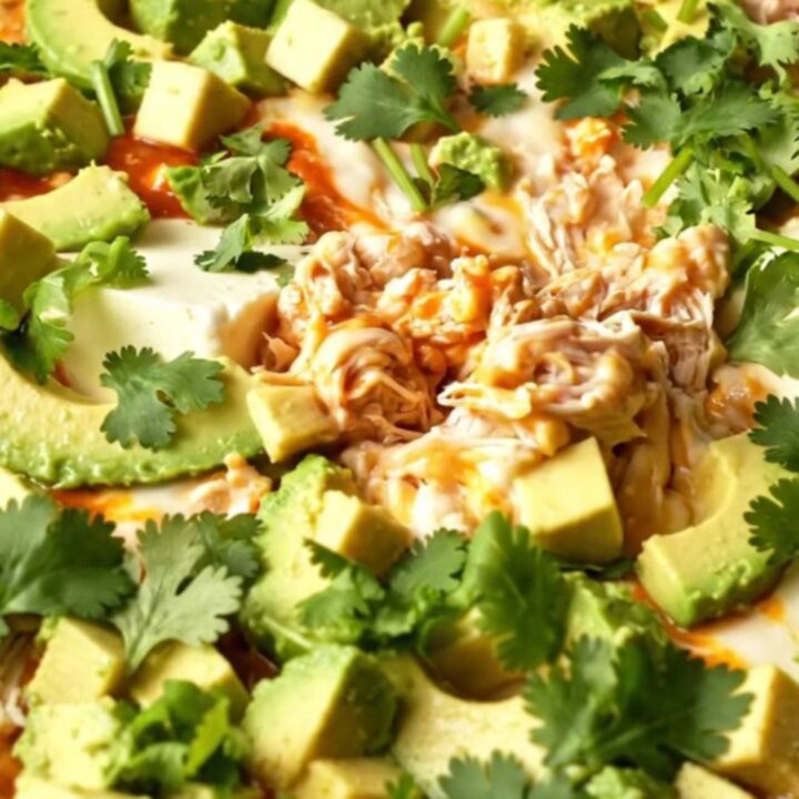 A close-up of a creamy chicken enchilada dip in a terracotta Crockpot with a dramatic cheese pull.
