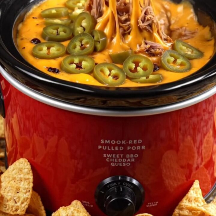 A close-up of a waffle-cut chip scooping up creamy BBQ pulled pork queso dip with a cheese pull.