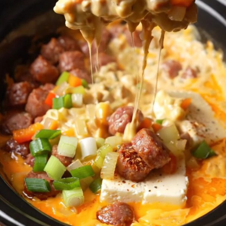 A close-up of a crusty baguette slice being dipped into a bubbling, creamy orange Cajun andouille queso dip.