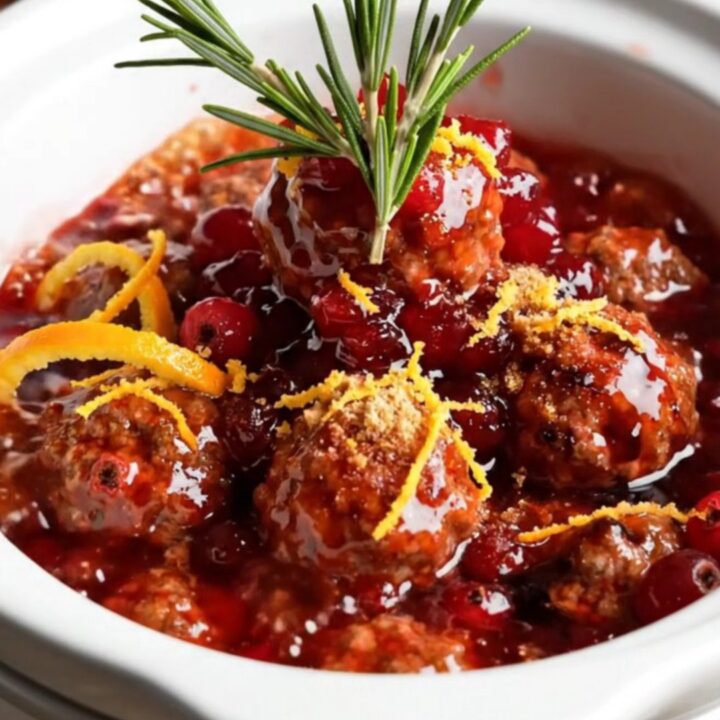 A ruby-glazed turkey meatball being lifted from a ceramic slow cooker with citrus glaze dripping.