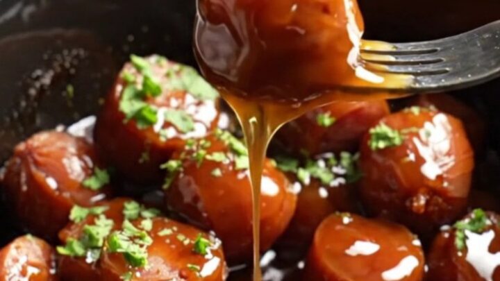 Close-up of sticky bourbon maple glazed kielbasa bites in a dark ceramic slow cooker, garnished with green parsley.