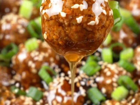 A close-up of sticky honey garlic meatballs in a black ceramic slow cooker, garnished with sesame seeds and scallions.