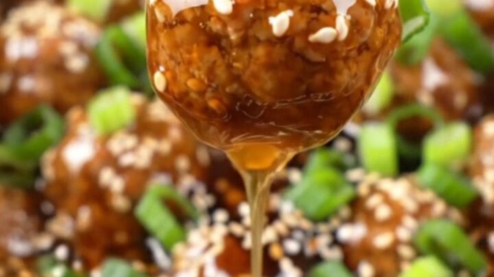 A close-up of sticky honey garlic meatballs in a black ceramic slow cooker, garnished with sesame seeds and scallions.