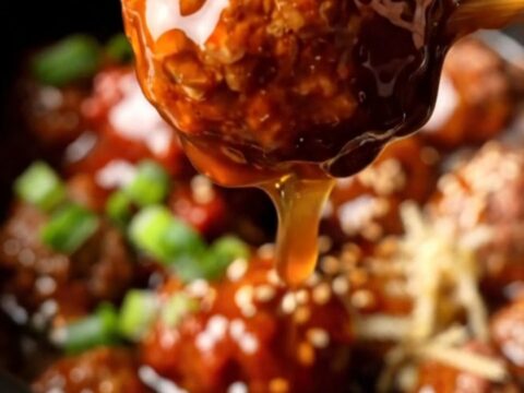A close-up shot of Korean-style beef meatballs glistening with a thick, crimson gochujang glaze in a dark charcoal crockpot.