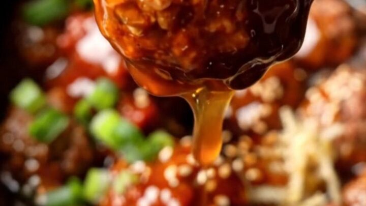 A close-up shot of Korean-style beef meatballs glistening with a thick, crimson gochujang glaze in a dark charcoal crockpot.